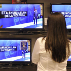 Una mujer observa los informativos en las televisiones de un centro comercial.