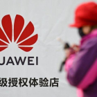 Una mujer consulta su smartphone junto a un cartel publicitario de Huawei, en una calle de Pekín.