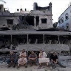 Cinco palestinos de Gaza sentados frente a un autobús y un edificio destruidos, en el 2014, por ataques aéreos israelís.
