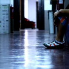 Un adolescente se oculta la cara sentado en el pasillo de su instituto.