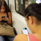 Dos chicas chatean por móvil en un vagón del metro de Barcelona.