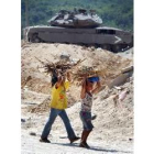 Dos niños palestinos pasan ante un tanque israelí cargados con leña