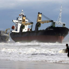 Un surfista pasa junto a los dos mercantes encallados en Valencia por el temporal.