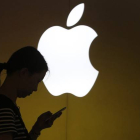 Una mujer mira su teléfono ante el logo de Apple en la tienda oficial de Shangai, China.