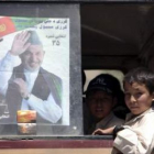 Varios niños miran por una ventana en la que hay un cartel electoral del presidente Hamid Karzai.