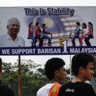 Un grupo de viandantes malasios caminan frente a un cartel de campaña del primer ministro de Malasia, Najib Razak, en Putrajaya.