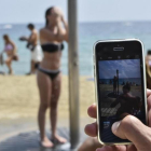 Una mujer se ducha en la playa de Barcelona delante de la cámara de un teléfono móvil.