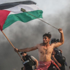 Un joven palestino tira piedras con una honda mientras con la otra mano lleva la bandera palestina.