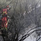 Un miembro de una brigada apaga los rescoldos para evitar que se reproduzca el fuego, en una zona de difícil acceso