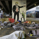 Un grupo de sin techo duerme bajo un puente de Sao Paulo ante una pintada de Bolsonaro como marioneta de Trump.