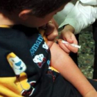 Un niño observa cómo le suministran la vacuna triple vírica.