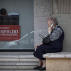 Una mujer mayor habla por teléfono móvil al lado de un cartel de planes de pensiones.