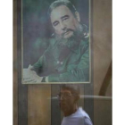 El retrato de Fidel Castro se refleja en una ventana de La Habana al paso de un ciudadano cubano