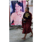 Un monje budista pasa frente a un cartel de Suu-Kyi.