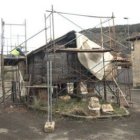 Un operario trabaja en el tejado de la estructura, rodeada de andamios para emprender su restauració