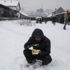 Un refugiado come en medio de la nieve en Belgrado.