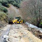 Una máquina retira maleza y piedras de la carretera que se llevó el Meruelo en Carracedo.