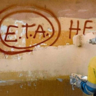 Una persona borra de una pared una pintada de apoyo a la banda terrorista que vive un triste final tras su derrota. DL