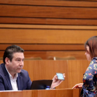 El procurador de UPL, Luis Mariano Santos, conversa con la procuradora de Podemos Lorena González durante la celebración del Pleno de las Cortes