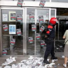 Una mujer intenta acceder a un centro comercial lleno de pegatinas, observada por un erzaina