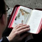 Un sacerdote lee un libro con la imagen del Papa Juan Pablo II como marcador.