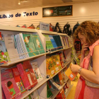 Una mujer observa libros de texto en el estante de una superficie comercial.