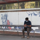 Un iraní espera en la parada de autobús junto a un mural contrario a Estados Unidos. MARINA VILLÉN