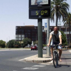 Un joven pasa con su bicicleta junto a un termómetro, expuesto al sol, que marca 50 grados en Córdoba.