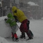 Dos niños juegan con una gigantesca bola de nieve en el casco urbano de Villablino