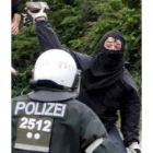 Un manifestante lanza una piedra contra un policía cargando