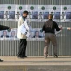 Un policía iraquí vigila a tres ciudadanos que colocan propaganda electoral en una calle de Bagdad