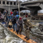 Un soldado ucraniano ayuda a civiles a cruzar el río bajo un puente destruido mientras huyen del asedio en la ciudad de Irpin. ROMAN PILIPEY