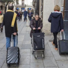 Una mujer pasa con su carrito de la compra entre dos turistas con sus maletas.