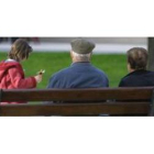 Una pareja de personas mayores observa a una niña que juega en un parque de León.