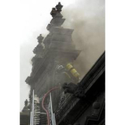 Un bombero intenta apagar las llamas subido en la fachada principal