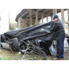 Uno de los vecinos levanta la lona que durante la mañana de ayer cubría el coche destrozado.