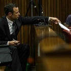 Oscar Pistorius entrega unas notas a uno de sus abogados, durante el juicio por asesinato que acoge el Tribunal Superior de Pretoria.