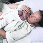 Una mujer acaricia a su hijo recién nacido en la cama de un hospital.