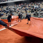 Varios operarios cubren con una lona la pista Philippe Chatrier donde jugaban Djokovic y Thiem.