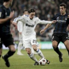Özil conduce el balón entre los jugadores de la Real Sociedad Xabi Prieto y Daniel Estrada.