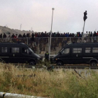 Inmigrantes encaramados en la valla de Melilla, con dos furgones de la Guardia Civil en primer término, este jueves.