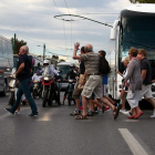 Un grupo de visitantes cruzan una calle de Atenas (Grecia) y saludan a los vehículos y motos que permanecen detenidos.