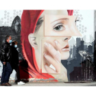 Una pareja, ayer por la mañana caminando por una calle de Ponferrada frente a un grafiti en el día del confinamiento perimetral. ANA F. BARREDO