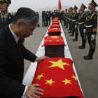 El embajador chino en Seul cubre los ataudes con la bandera de China, durante la ceremonia.