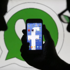 Un hombre muestra el logotipo de Facebook en un móvil con el de la aplicación de mensajería instantánea WhatsApp al fondo.