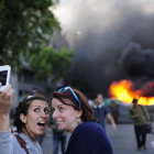 Unas turistas se hacen un 'selfie' con unos contenedores ardiendo de fondo este jueves, en Barcelona.