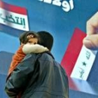 Un padre pasa con su hija en brazos por delante de un cartel electoral en Bagdad