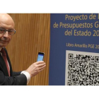 El ministro de Hacienda, Cristóbal Montoro, escanea con el móvl el código QR del proyecto de Ley de Presupuestos Generales del Estado (PGE) para 2017, poco antes de la rueda de prensa que ha ofrecido hoy en el Congreso para presentarlo.
