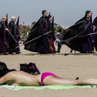 Bañistas y participantes en una procesión de Semana Santa, en la playa de Valencia.