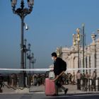 Un joven con su maleta y mascarilla pasa ante el Palacio Real de Madrid, vallado. JUAN CARLOS HIDALGO